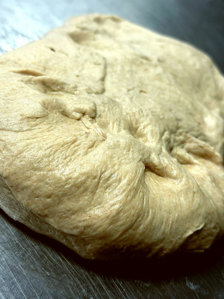 A rested ball of sourdough on a steel bench, surface taut and glossy
