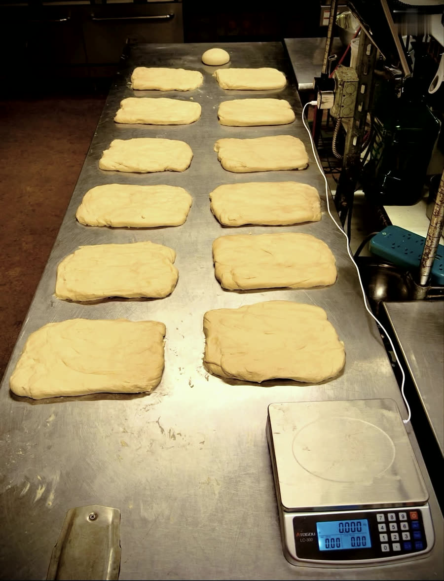 Rows of hand-shaped dough pieces laid out on a steel bench
